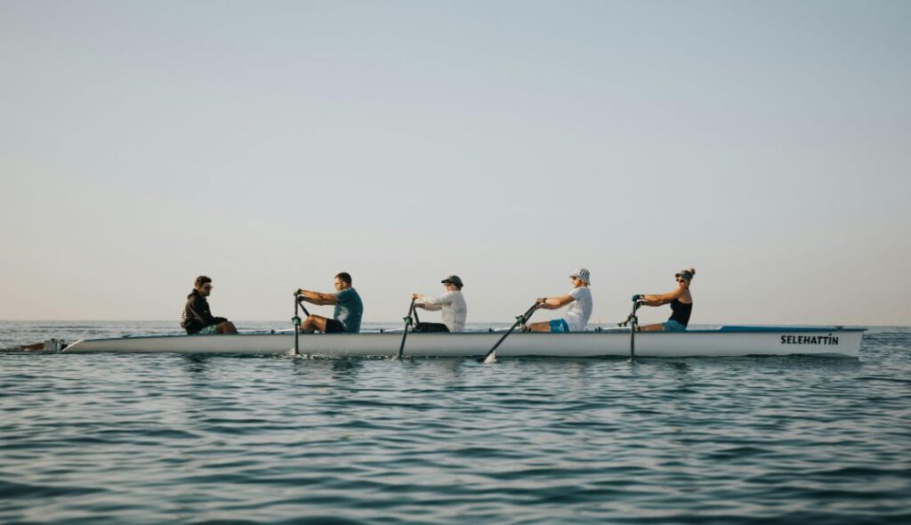 Unterschiedliche Menschen sintzen gemeinsam in einem Boot auf offener See.